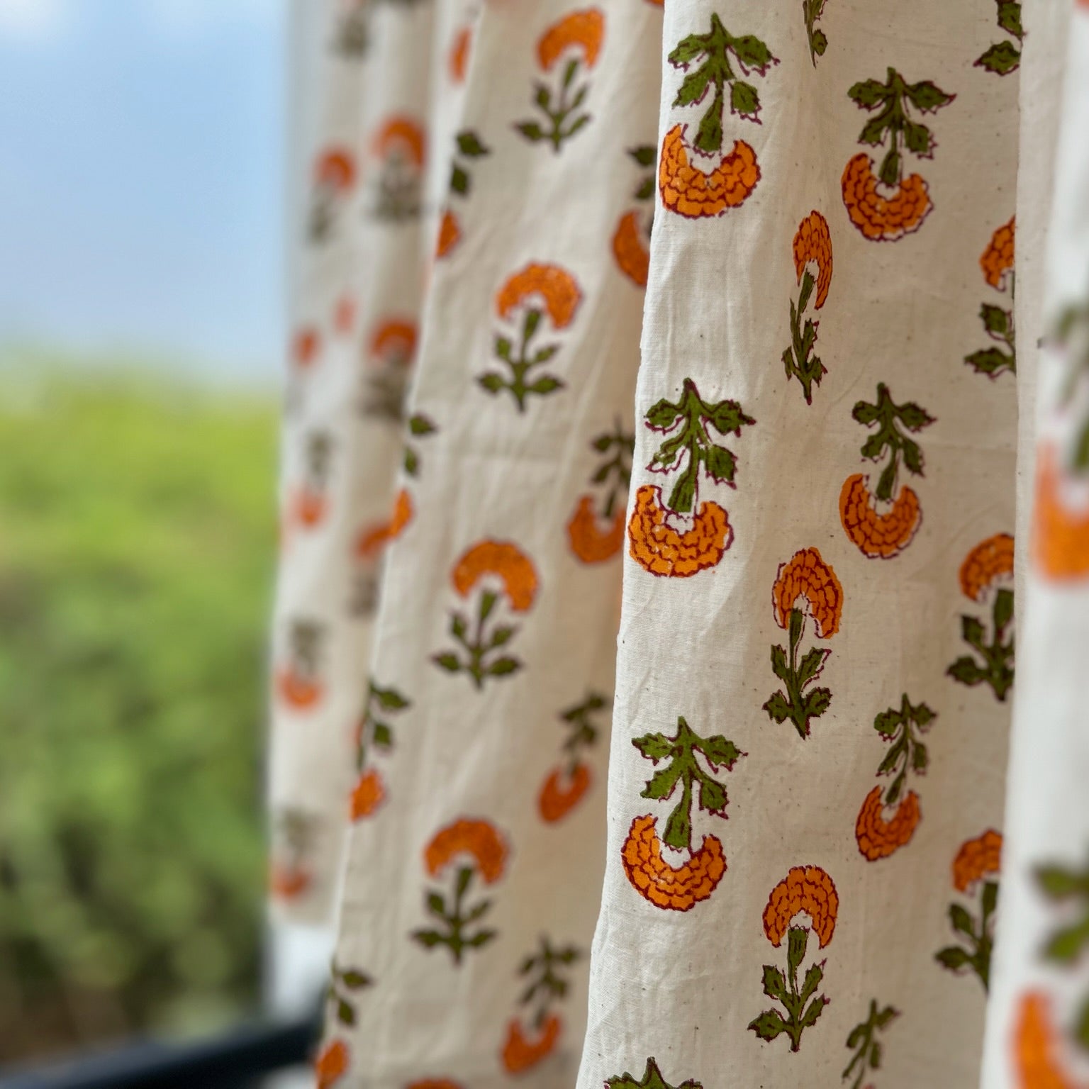 Curtains with orange and green pattern in front of a blurred outdoor background