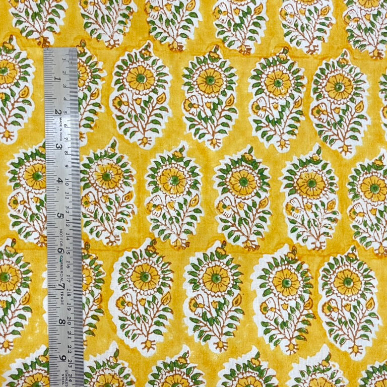 Fabric with a floral pattern on a yellow background, measured by a ruler.