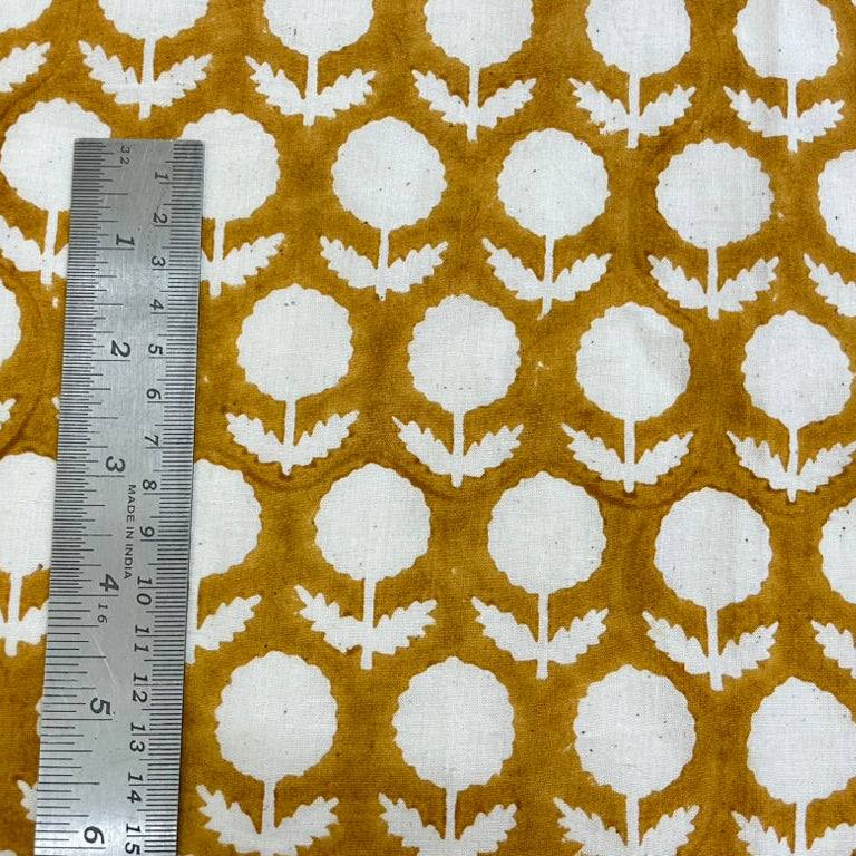 Fabric with white floral pattern on a mustard background, measured by a ruler.