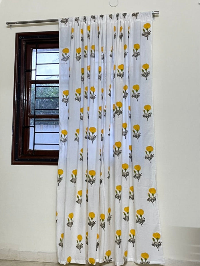 Curtain with yellow floral pattern hanging in front of a window.