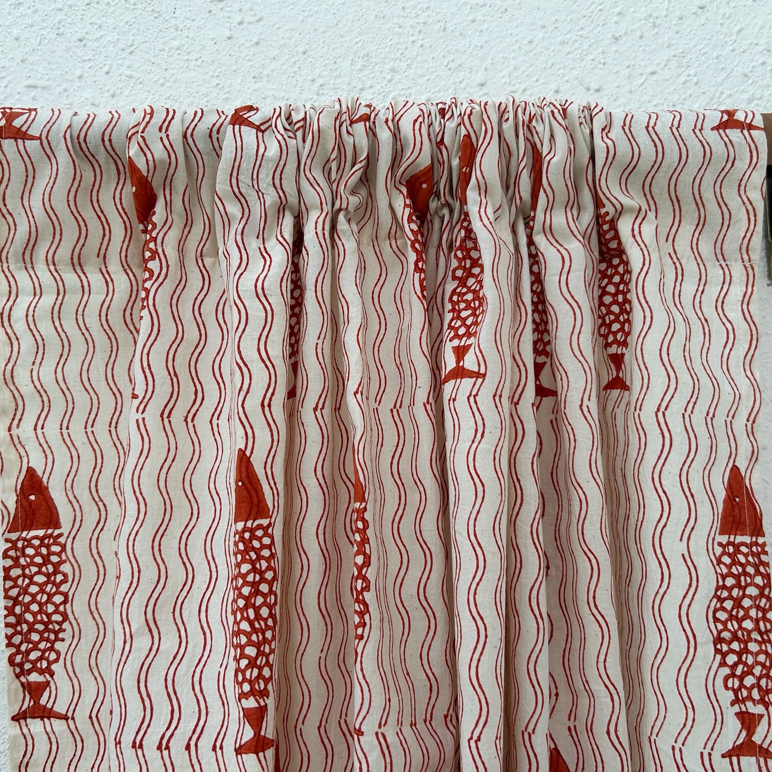 Curtain with red fish pattern on a wooden rod against a white wall