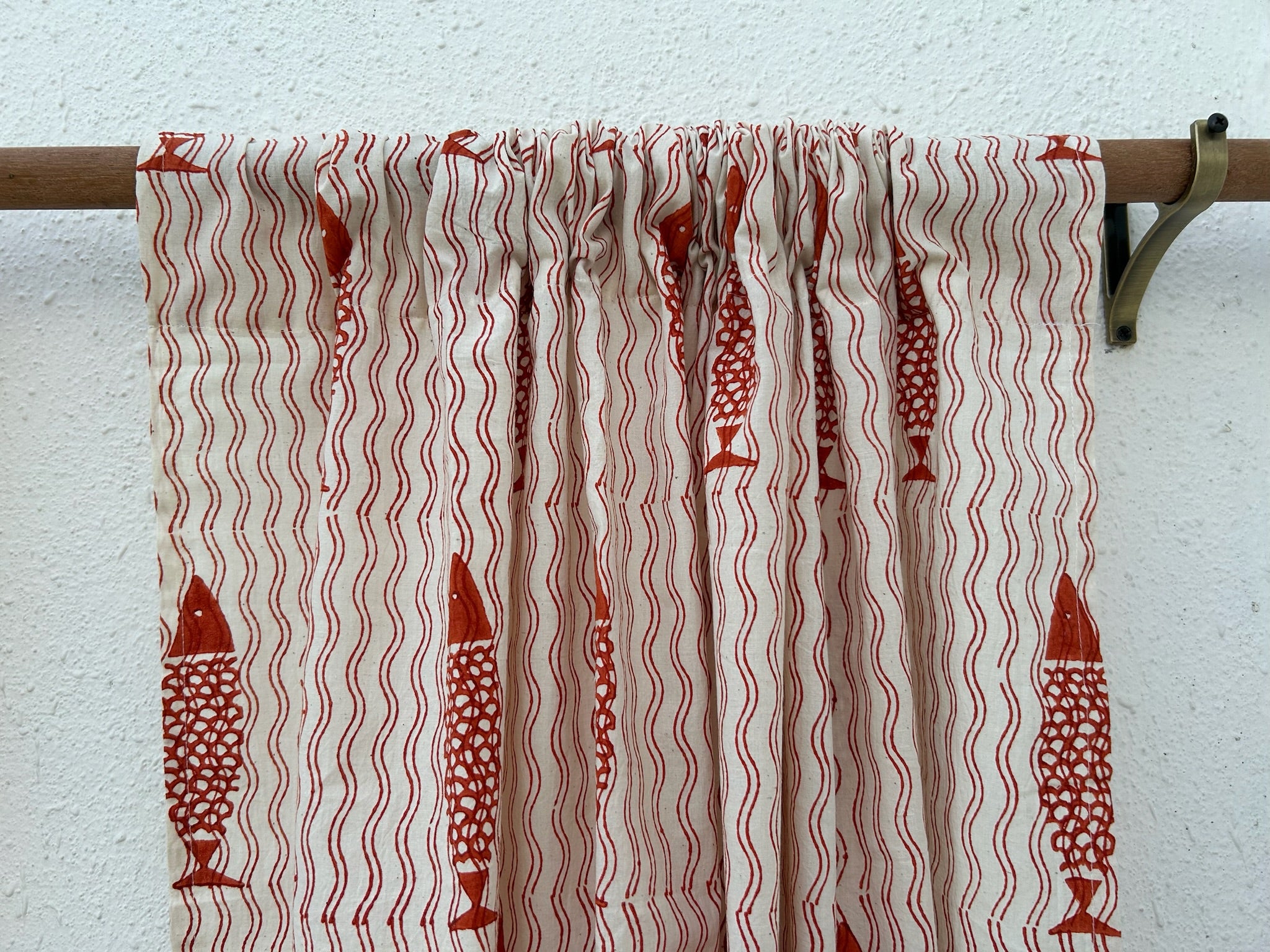 Curtain with red fish pattern on a wooden rod against a white wall