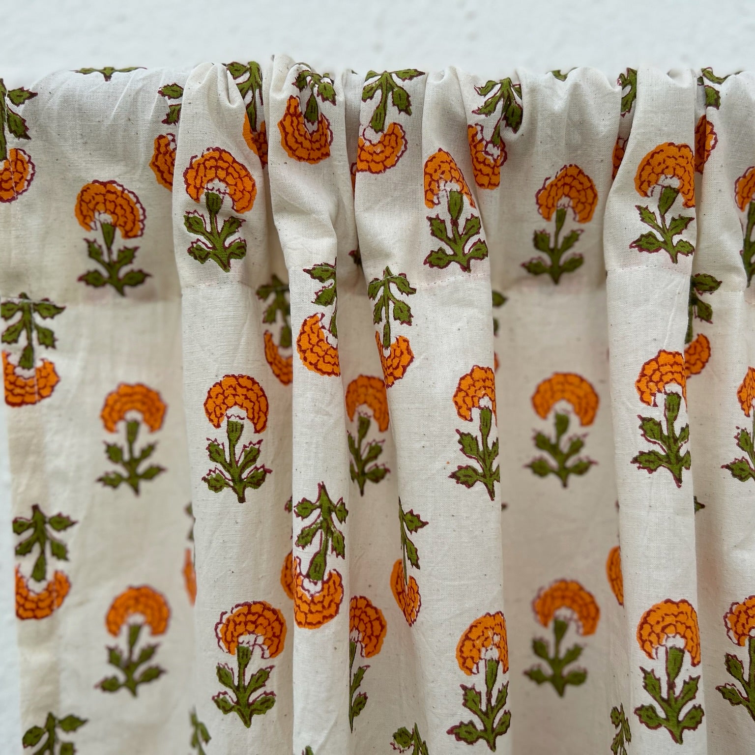 Fabric with orange and green floral pattern draped over a wooden rod against a white background