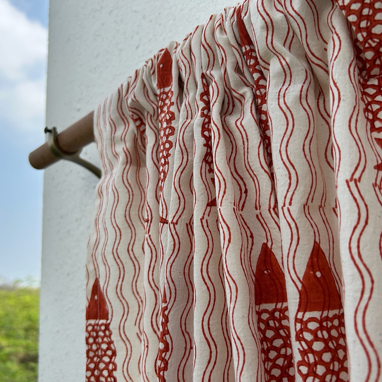 Red and white patterned fabric on a clothesline with a blue sky and greenery in the background