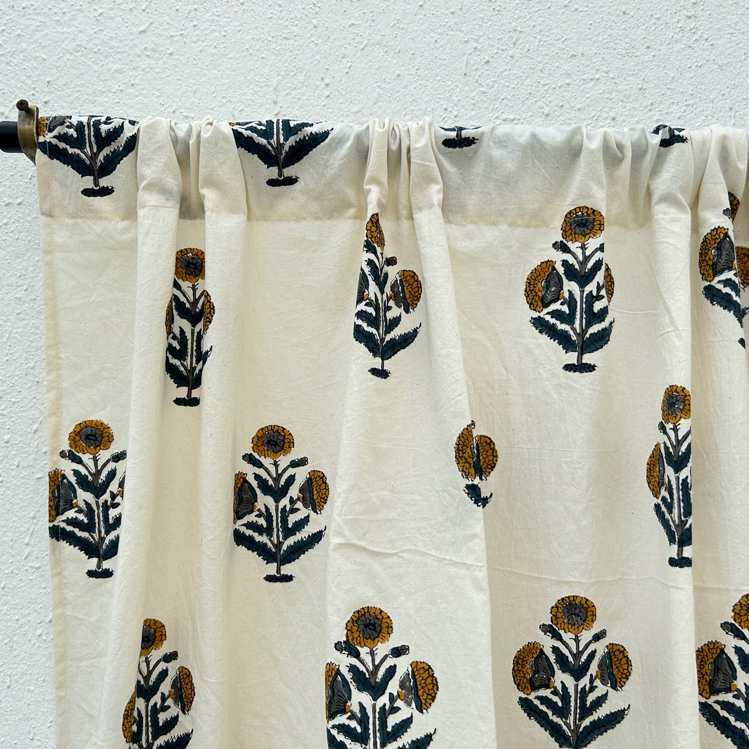 White curtain with black and brown floral patterns hanging against a white wall.