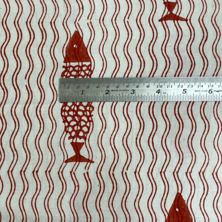 Fabric with red fish pattern and wavy lines, measured by a ruler.