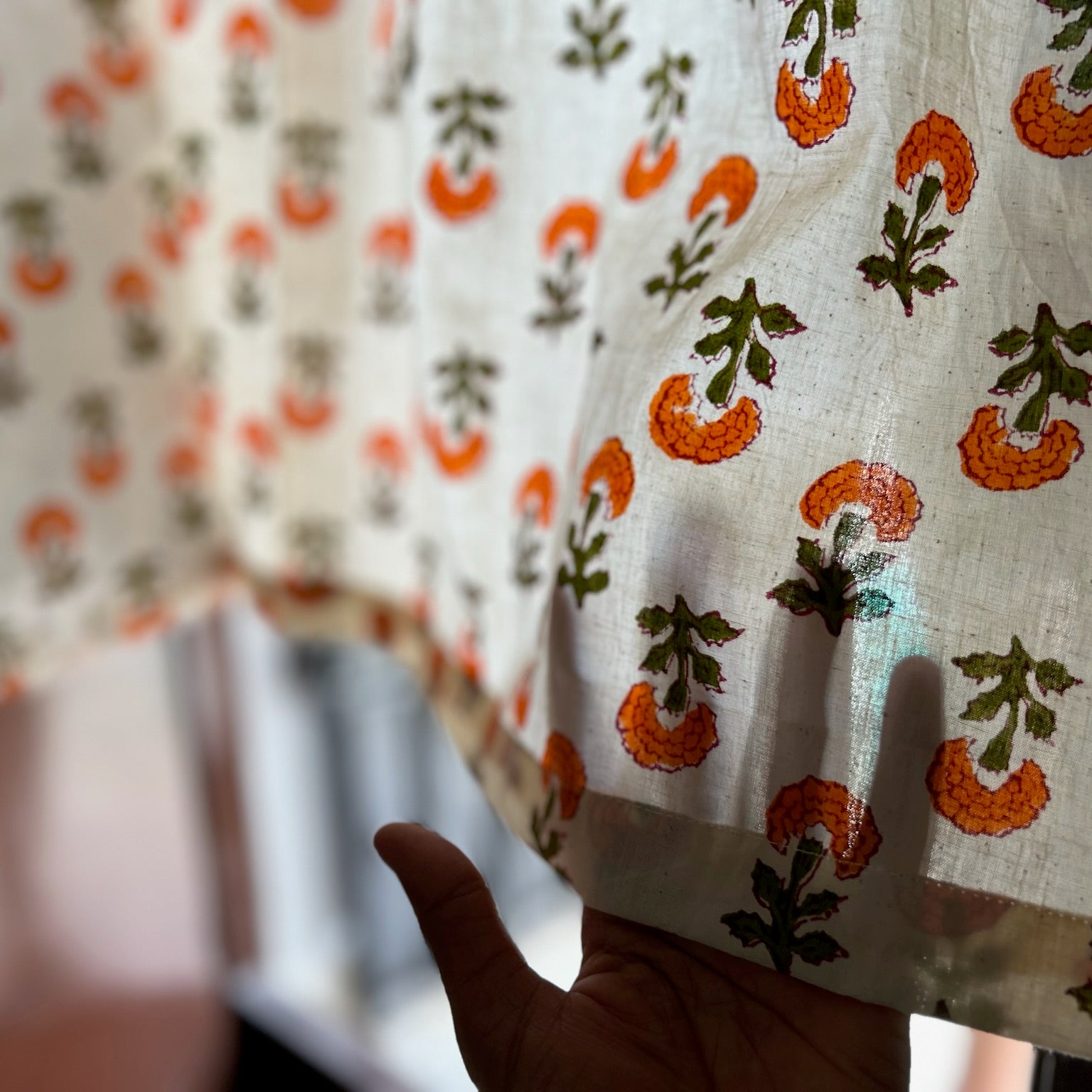 Close-up of a hand holding a piece of fabric with orange and green floral pattern.