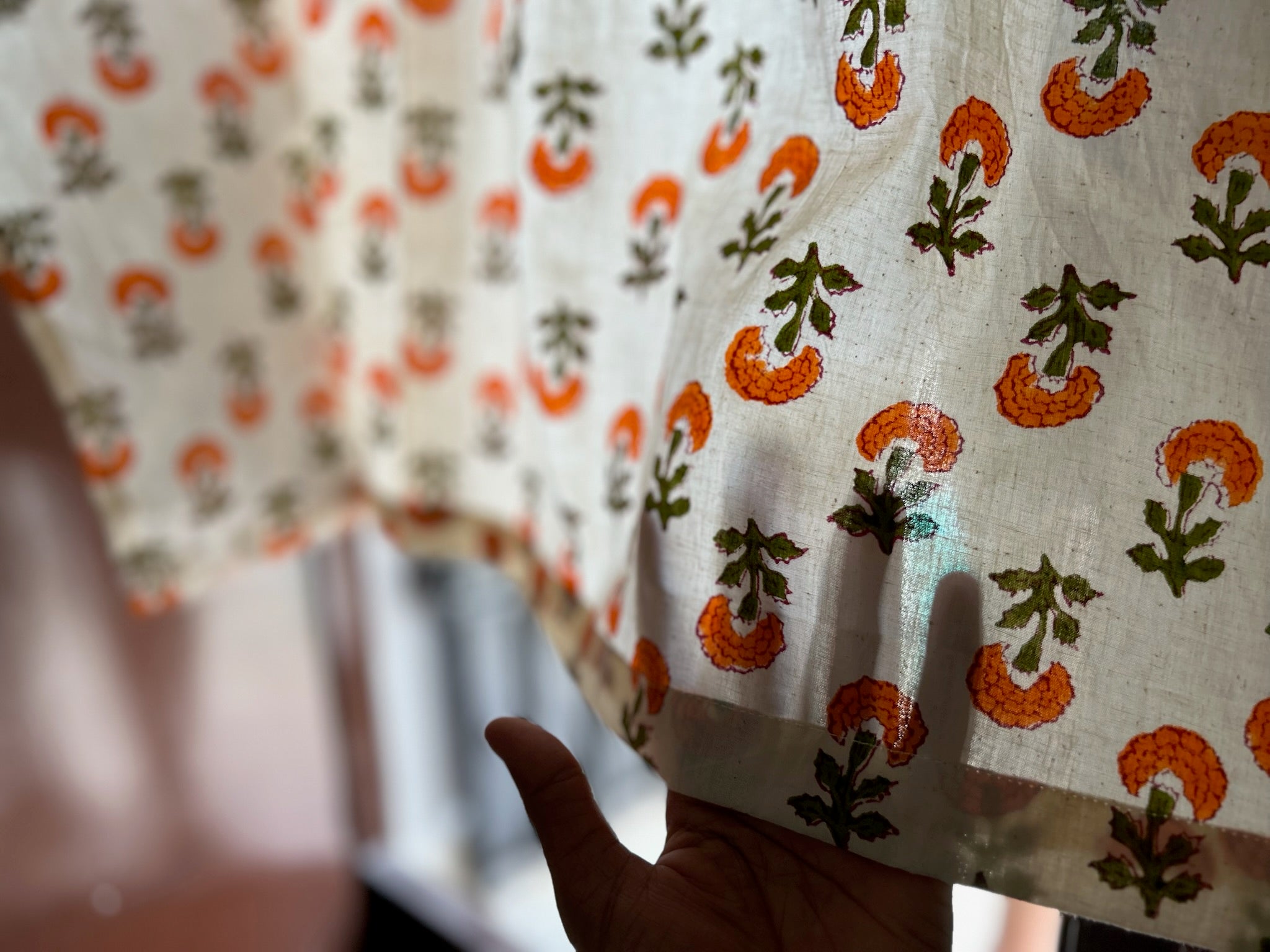 Close-up of a hand holding a piece of fabric with orange and green floral pattern.
