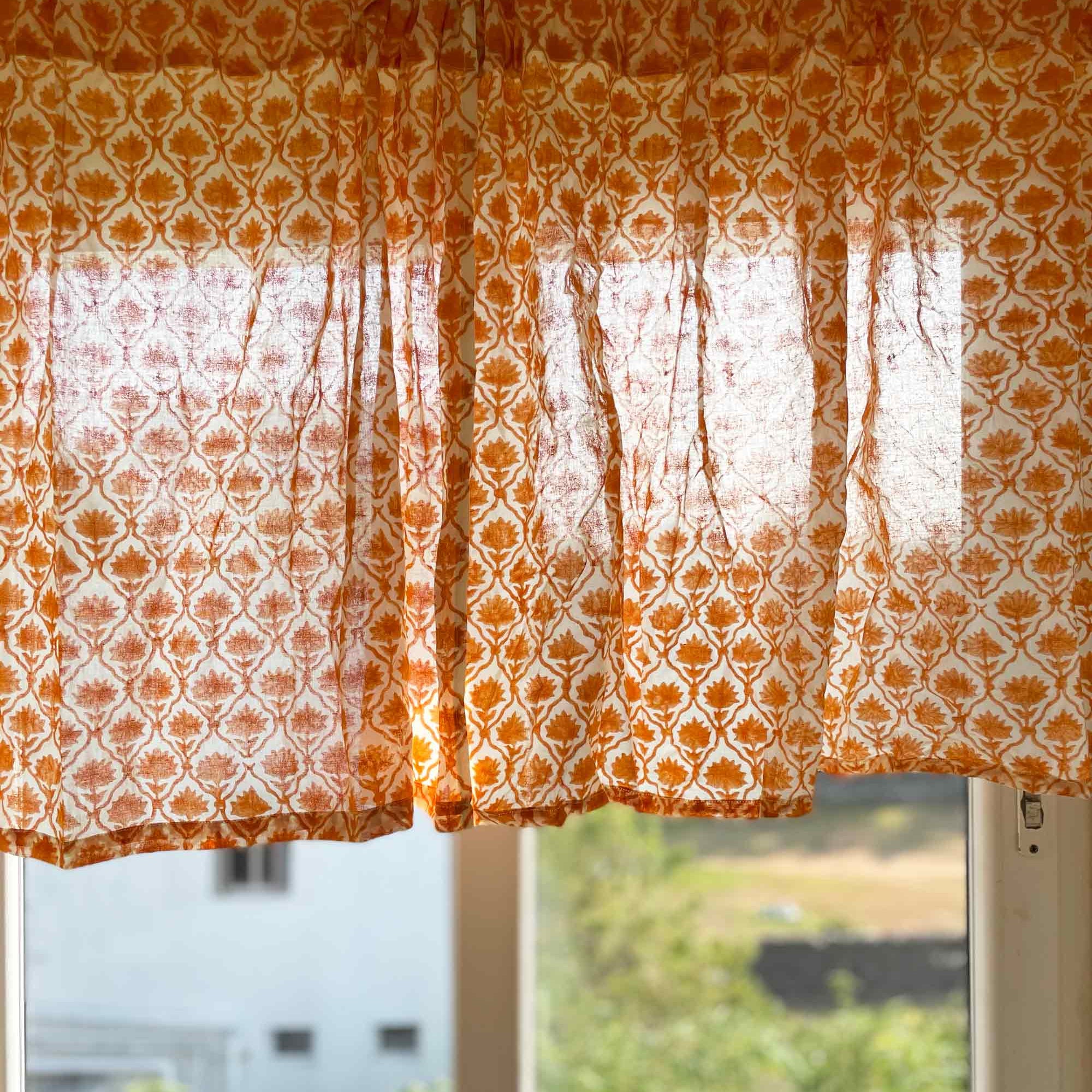 Orange patterned curtain with lace overlay in front of a window