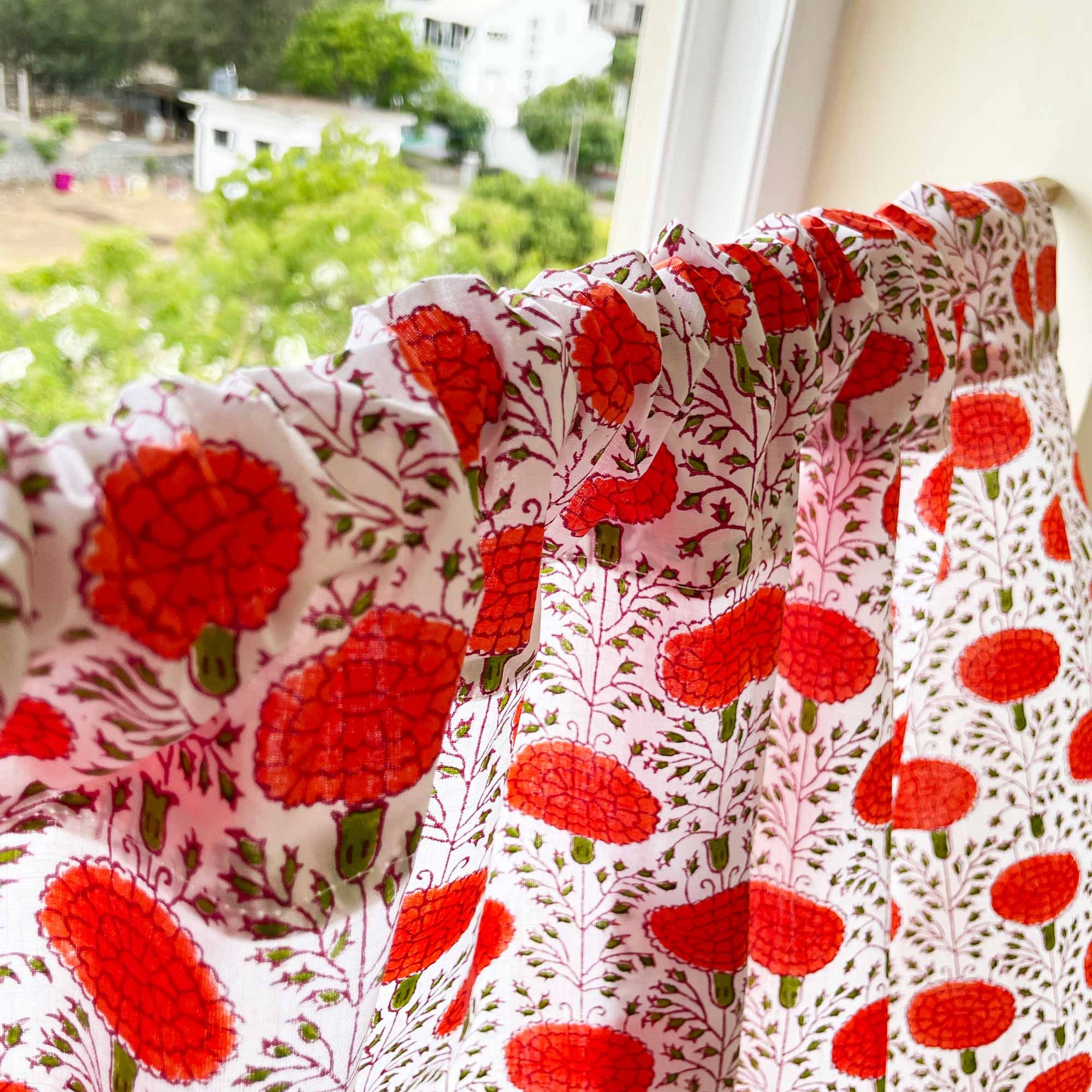 Floral patterned fabric with red flowers on a white background, hanging by a window.