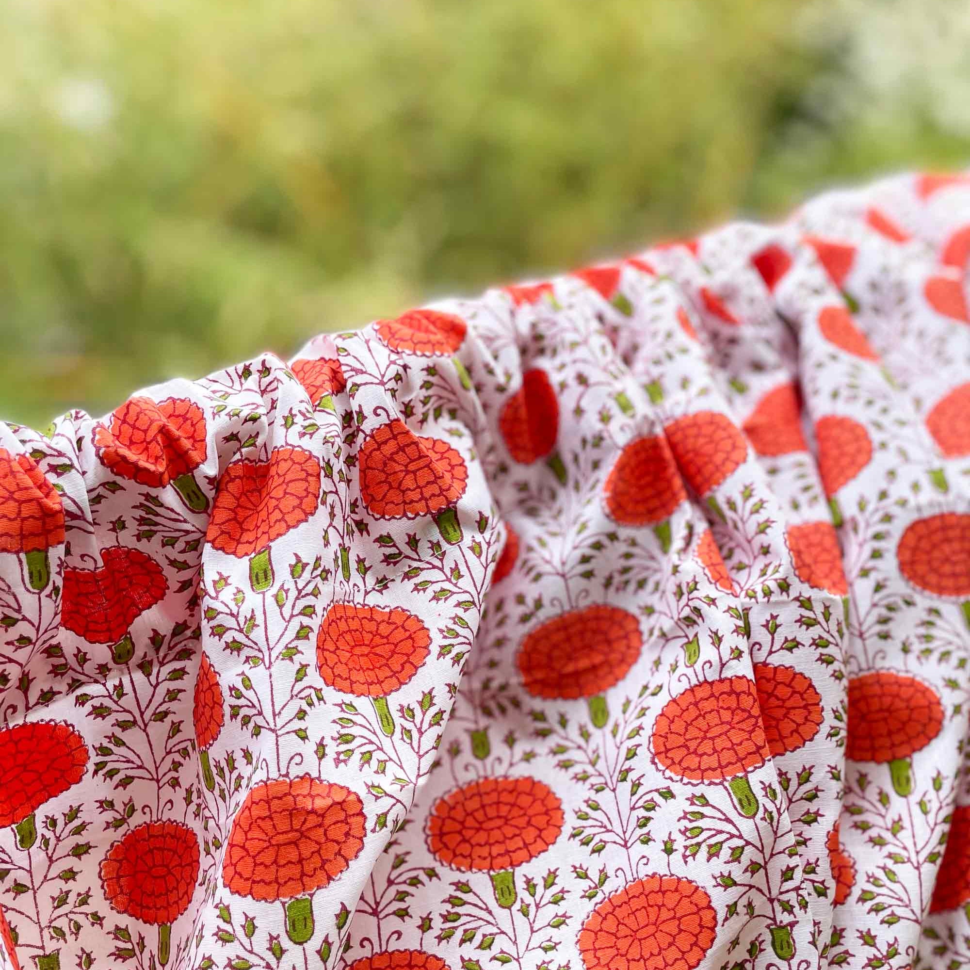Close-up of fabric with red floral pattern against a blurred natural background
