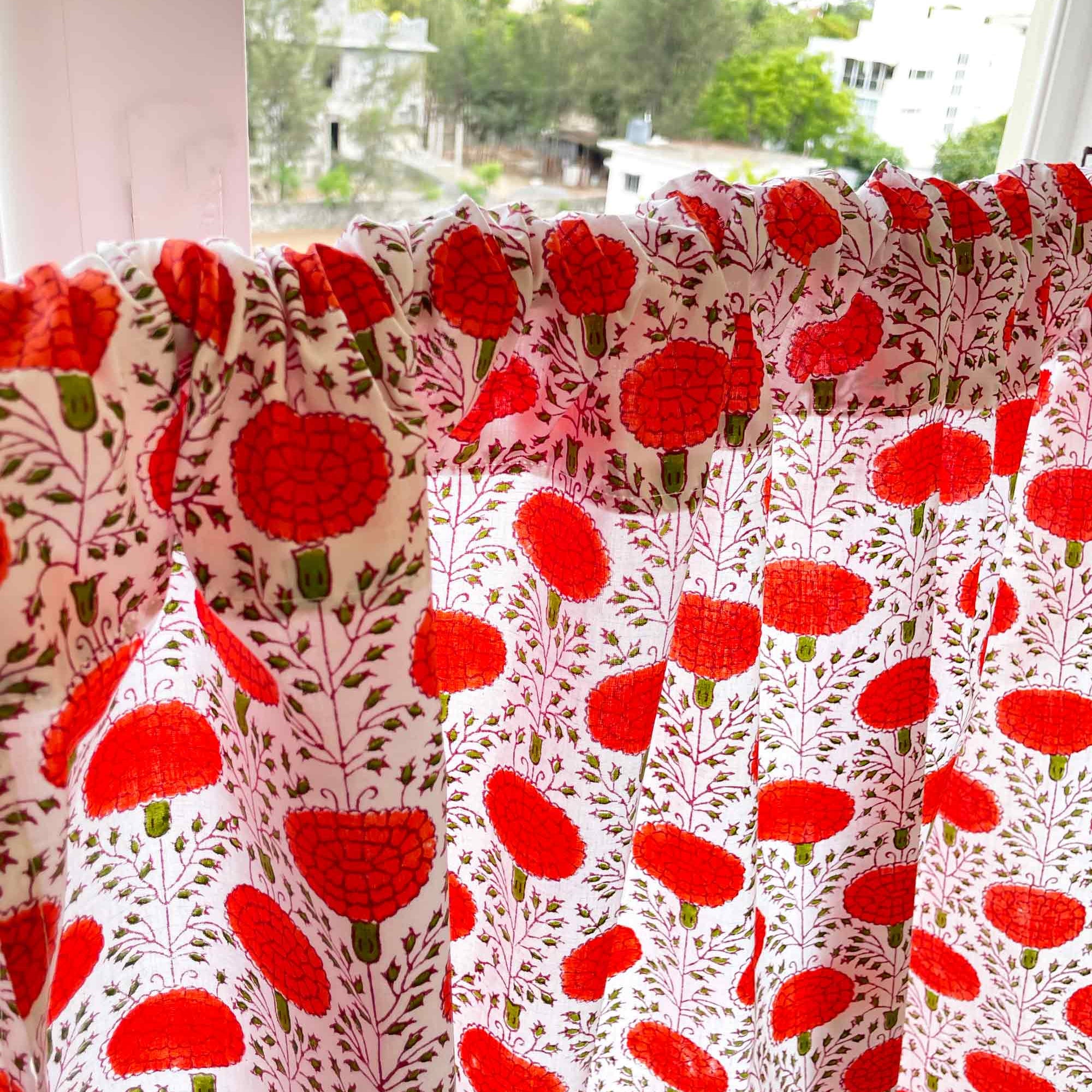 Red floral patterned fabric draped over a window with a view of greenery outside.