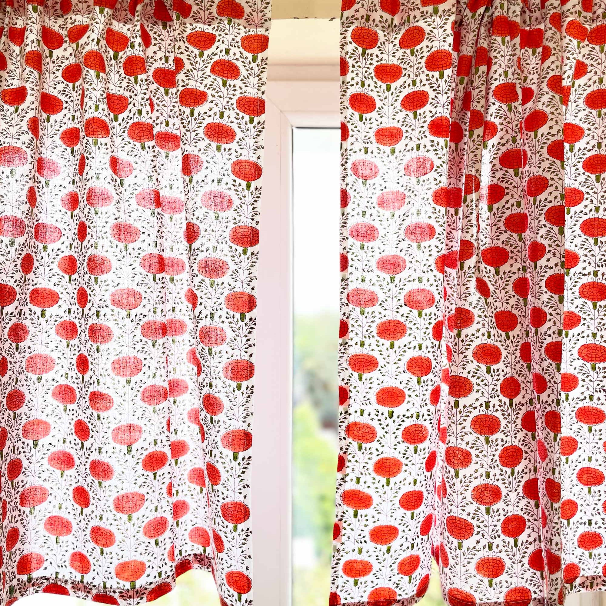 Red and white patterned curtains on a window with blurred greenery in the background.