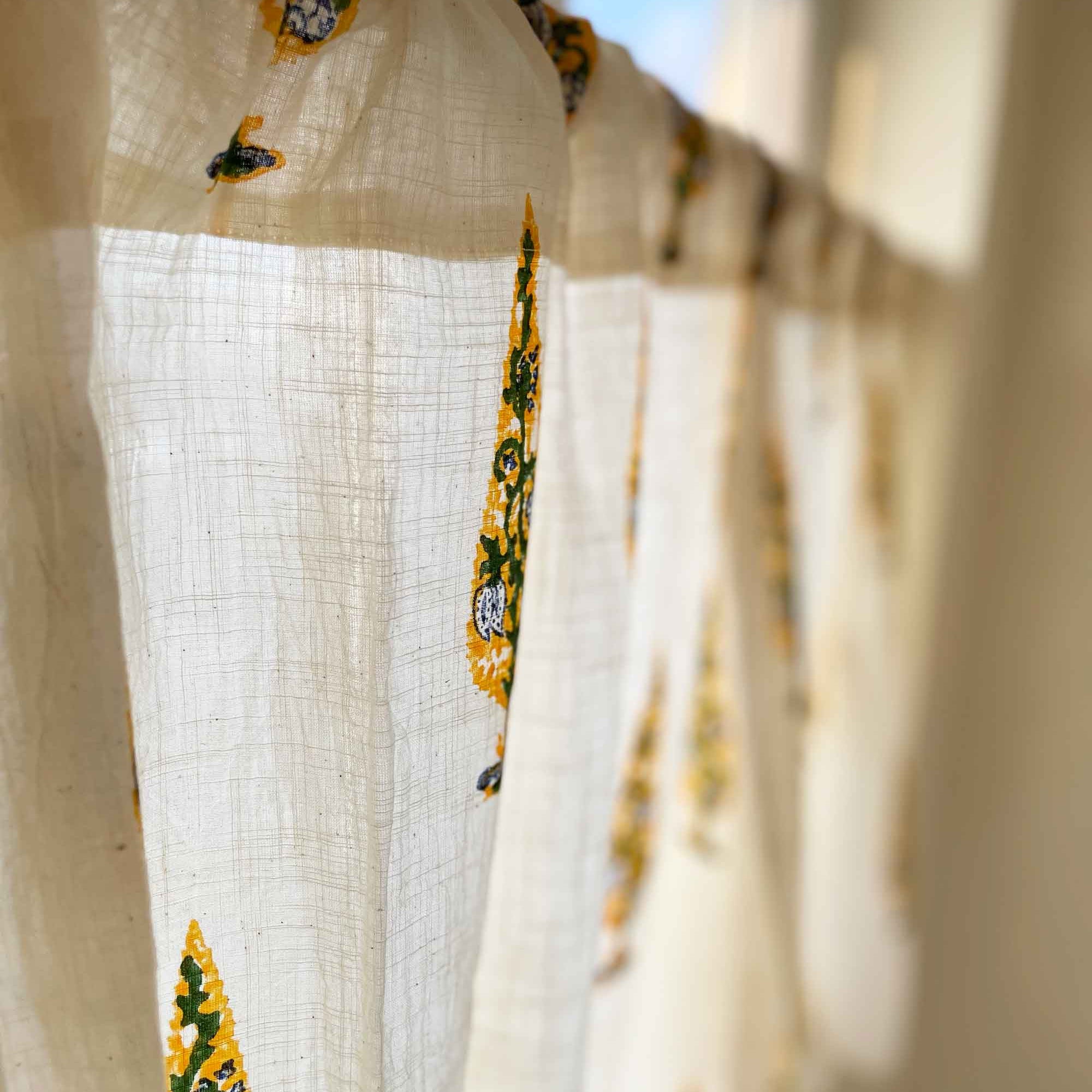 White fabric with yellow floral patterns hanging against a bright background