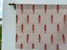 Textile with red fish pattern on a beige background, hanging against a white wall.