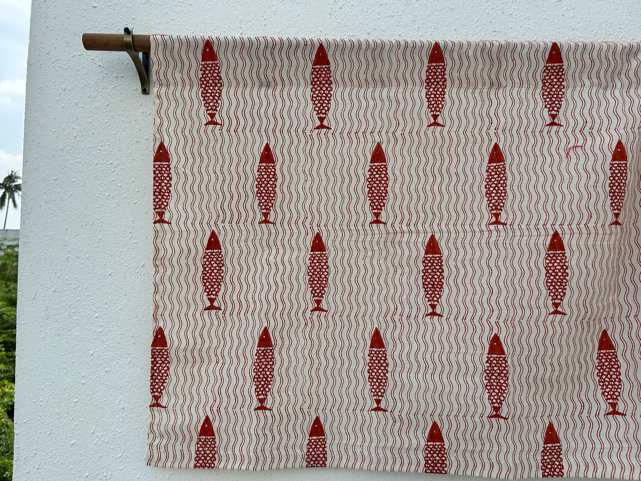 Textile with red fish pattern on a beige background, hanging against a white wall.