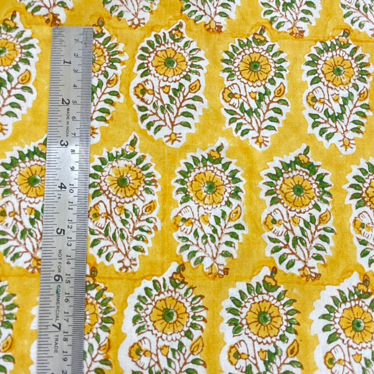 Fabric with floral patterns on a yellow background, measured by a ruler.