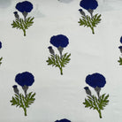 White fabric with a repeating block-print pattern of dark blue marigold flowers and green leaves.
