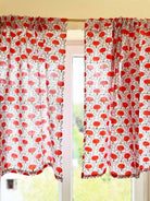 Red and white patterned curtains on a window with blurred greenery in the background.