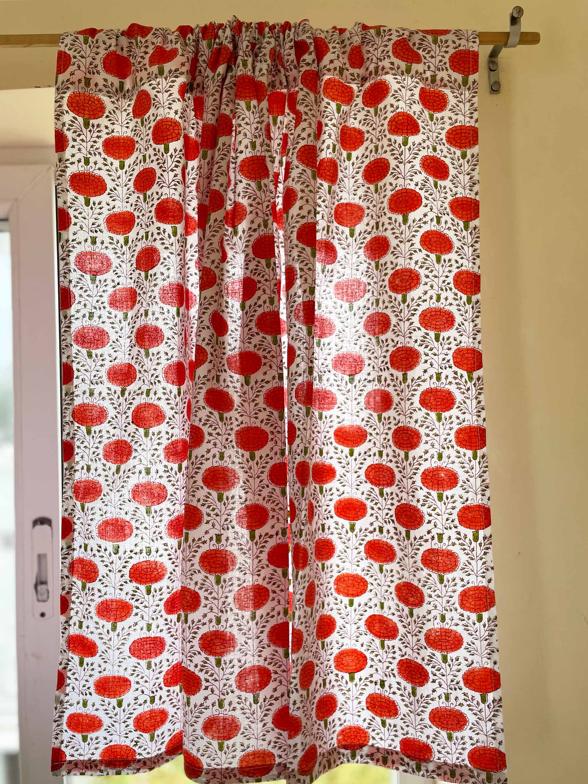 Curtain with red floral pattern hanging on a wooden rod against a beige wall.